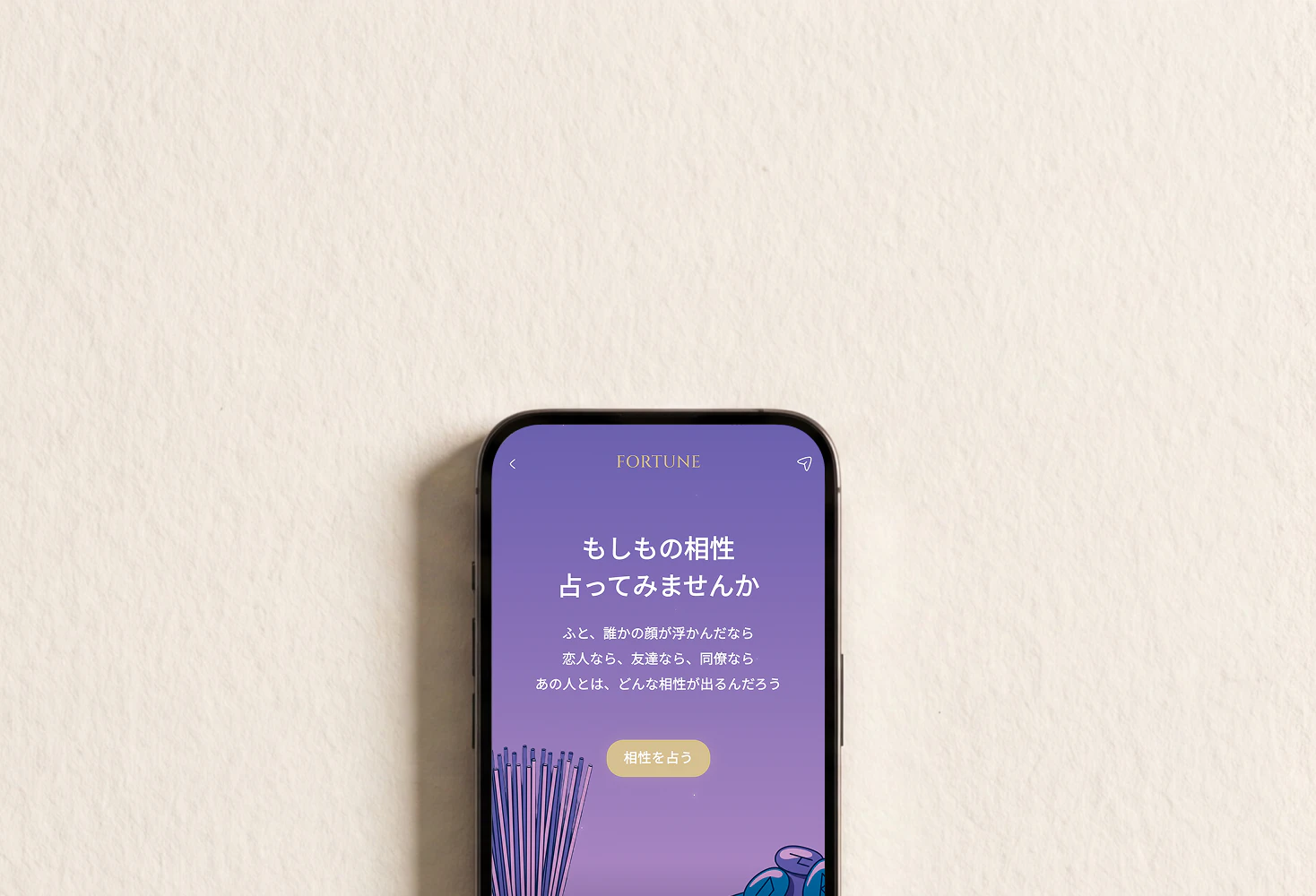 壁の前のスマートフォンに映る、相性占いのはじめの画面。